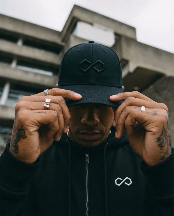 Homme portant casquette et hoodie noirs au logo minimaliste, style urbain lifestyle