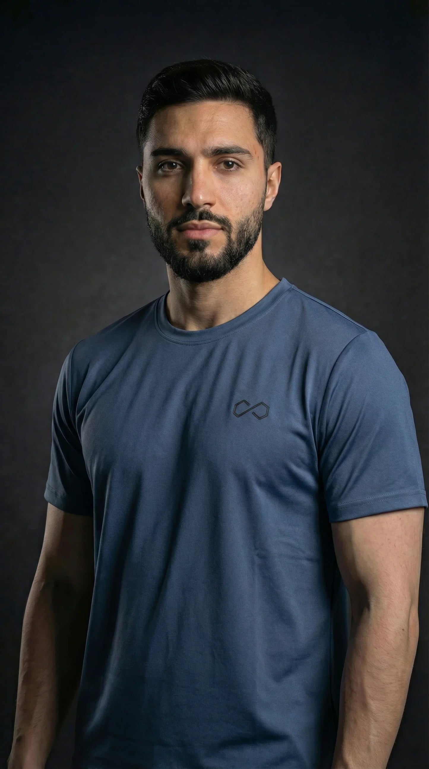 Homme portant un t-shirt sport bleu minimaliste à logo discret, fond foncé.