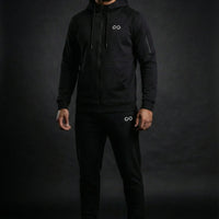 Homme portant un ensemble de survêtement noir minimaliste avec logo infini, fond sombre.