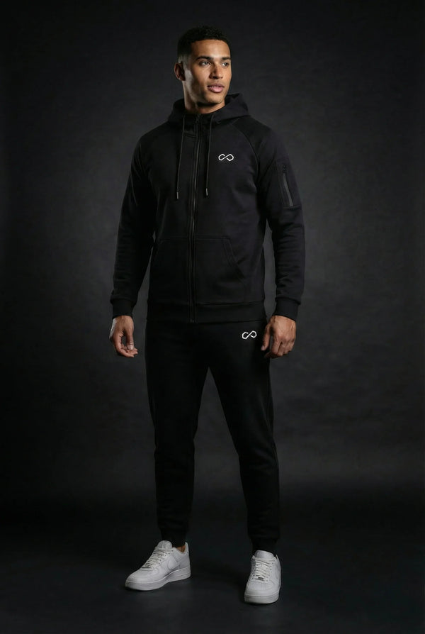 Homme portant un ensemble de survêtement noir minimaliste avec logo infini, fond sombre.