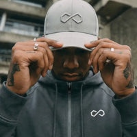 Homme portant une casquette grise et un hoodie gris foncé avec logo infini, style urbain