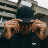 Homme portant casquette et hoodie noirs au logo minimaliste, style urbain lifestyle