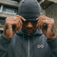Homme portant un bonnet gris minimaliste et un hoodie zippé dans un décor urbain