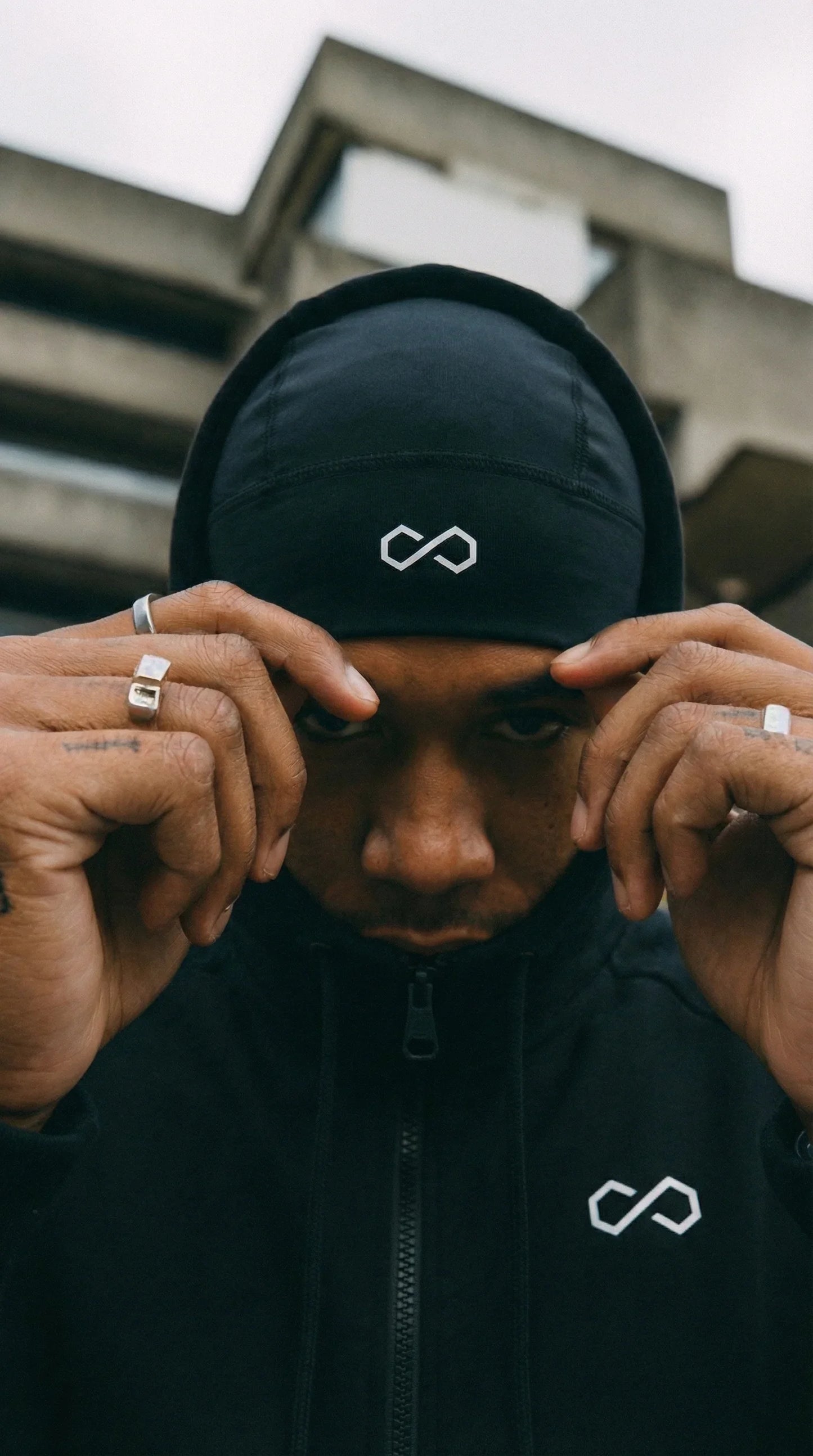 Homme portant un bonnet noir sport avec logo blanc et sweat à capuche, style urbain