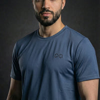Homme portant un t-shirt sport bleu minimaliste à logo discret, fond foncé.