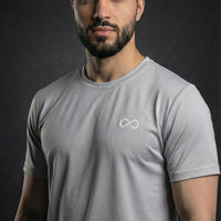 Homme portant un t-shirt sport gris à col rond, logo minimaliste blanc sur la poitrine.